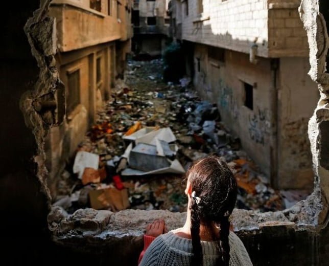 TOPSHOT - Shatha, the daughter of 48-year-old Palestinian refugee Issa al-Loubani, looks out the window of their apartment in the Palestinian Yarmuk camp, on the southern outskirts of the Syrian capital Damascus, on November 25, 2020. - When Syrian authorities said they would allow returns to the war-ravaged Yarmuk camp for Palestinian refugees in southern Damascus, Issa al-Loubani rushed to sign up and quickly started repairing his home. Loubani, who first left in 2012, is determined to join their ranks even if the windows of his wrecked apartment are still covered with plastic sheeting. (Photo by LOUAI BESHARA / AFP) (Photo by LOUAI BESHARA/AFP via Getty Images)