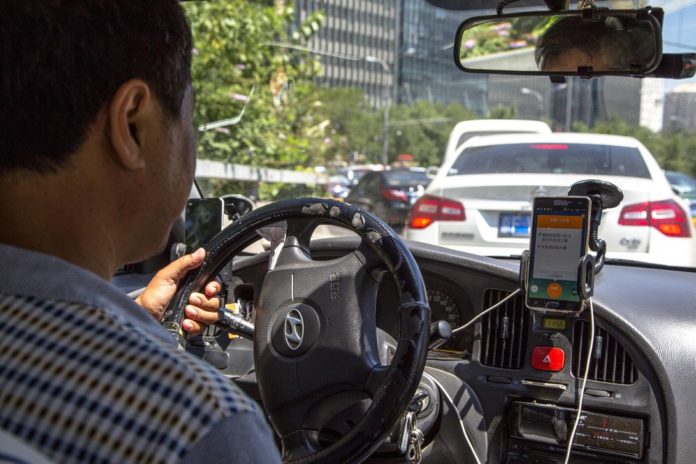 A taxi driver is using Didi Dacha App while driving on the