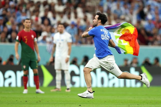 A pitch invader with a Pride flag runs across the pitch during an World Cup match between Portugal and Uruguay. 