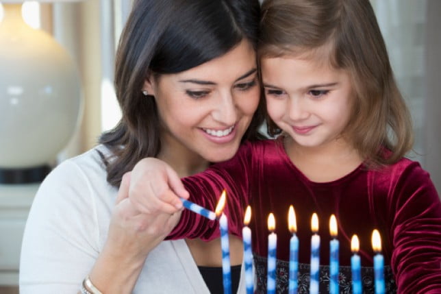 A woman lighting the Chanukah menorah with her daughter