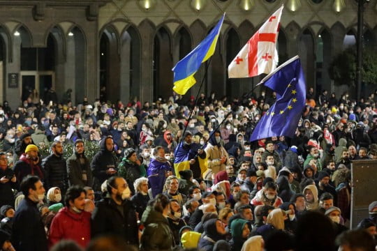 Protesters wave Ukrainian, Georgian and EU flags as they gather outside the Georgian parliament building in Tbilisi, Georgia, Wednesday, March 8, 2023. Georgian authorities used tear gas and water cannon outside the parliament building in the capital Tuesday against protesters who oppose a proposed law some see as stifling freedom of the press. (AP Photo/Zurab Tsertsvadze)